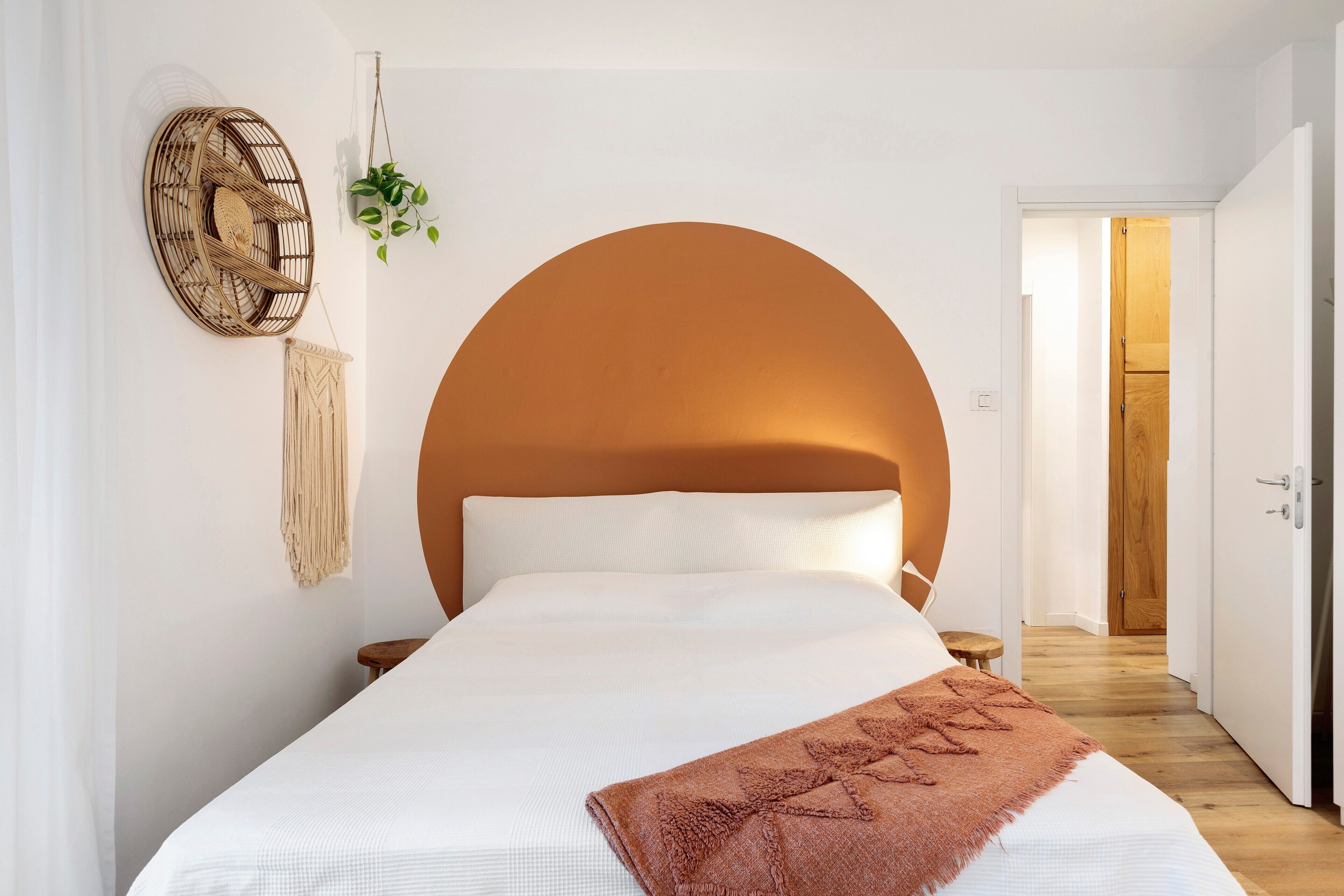 A bedroom with a large bed, a round wall headboard, a macrame wall hanging, and a wooden door.