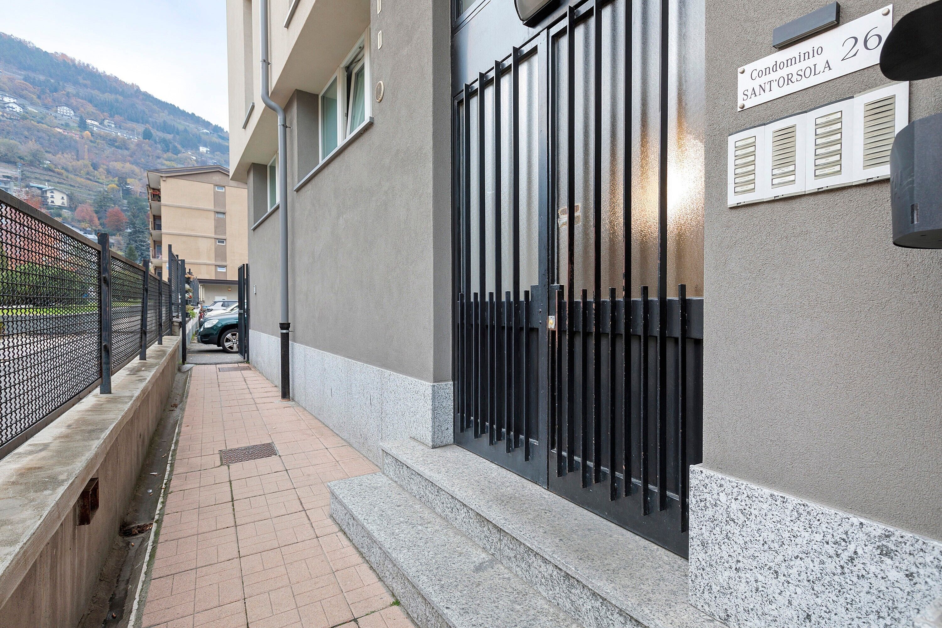 A building with a gated entrance, a sign indicating 'Condominio Santorsola 26,' and a paved walkway.