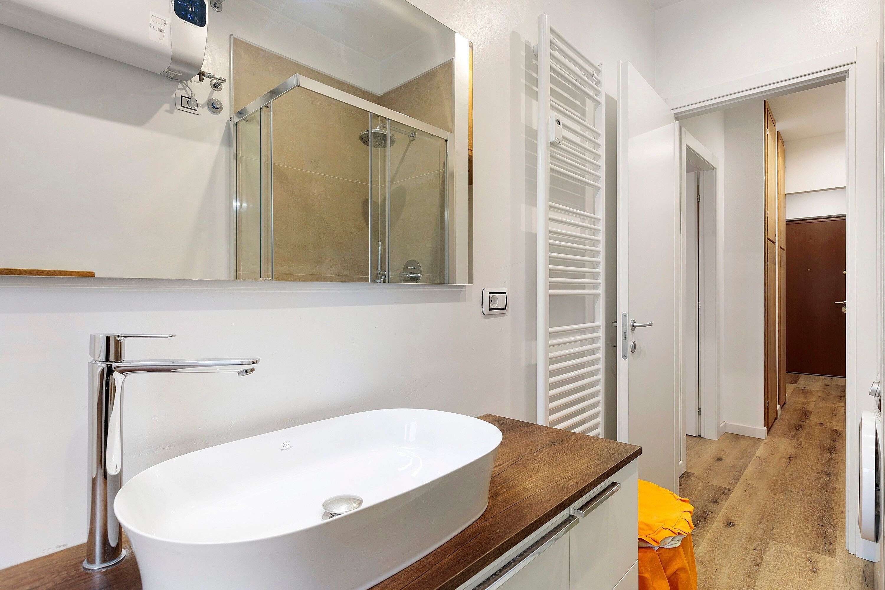 Un baño con lavamanos blanco, grifo cromado y cabina de ducha con mampara de vidrio.