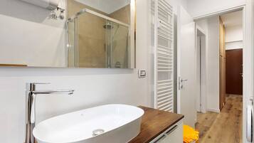 Un baño con lavamanos blanco, grifo cromado y cabina de ducha con mampara de vidrio.
