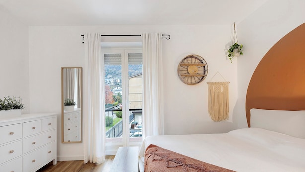 Une chambre à coucher comprenant un lit, un banc, une commode, un miroir et une vue sur l’extérieur.