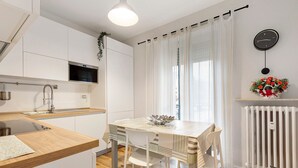 Une cuisine moderne avec des meubles blancs, un plan de travail en bois, un four à micro-ondes encastré et un coin repas avec une table et des chaises blanches.