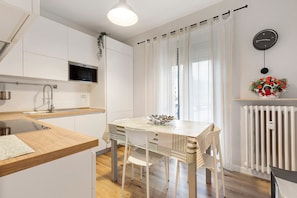Una cucina moderna con mobili bianchi, un piano di lavoro in legno, un microonde integrato e una zona pranzo con tavolo e sedie bianche.