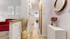 Un couloir avec un canapé rouge, une console blanche surmontée d’un vase et un miroir encadré en bois.