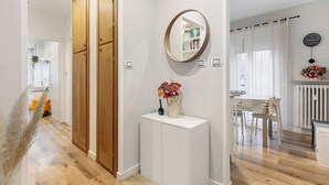 Un couloir avec une armoire en bois, une console blanche ornée d’un vase, un miroir et un coin repas avec des chaises et une table.