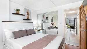 A hotel room with a large bed, a mirror, a small desk, and a view of the outdoor area. - 7th Fl Aloha Lani  | Lanai | AC | Parking | Pool (Honolulu)