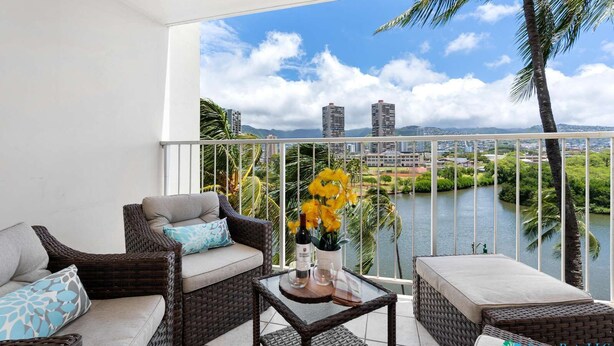 A balcony with wicker furniture, a glass table, and a vase of yellow flowers. - 7th Fl Aloha Lani  | Lanai | AC | Parking | Pool (Honolulu)