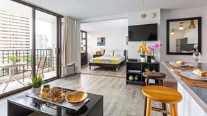 Et moderne hotelværelse med stor balkon, seng med gul og hvid dyne, fladskærms-tv, spiseplads med bar samt udsigt over bybilledet.