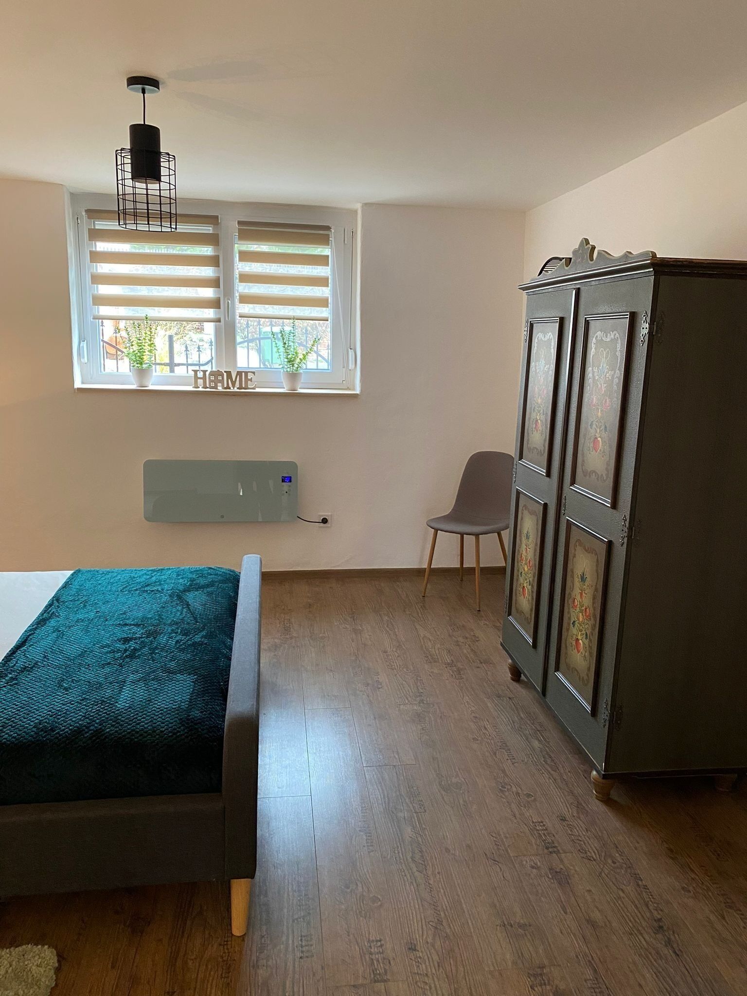 A bedroom with a bed, a wardrobe, a chair, and a window with blinds.