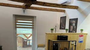 A cozy room with a wooden ceiling, a small kitchenette, a door leading to an outdoor area, and a few potted plants. - The Hungarian Valley (Szellő)