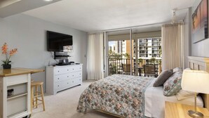 Une chambre d’hôtel avec un lit, un bureau, une télévision et un balcon donnant sur les bâtiments environnants.