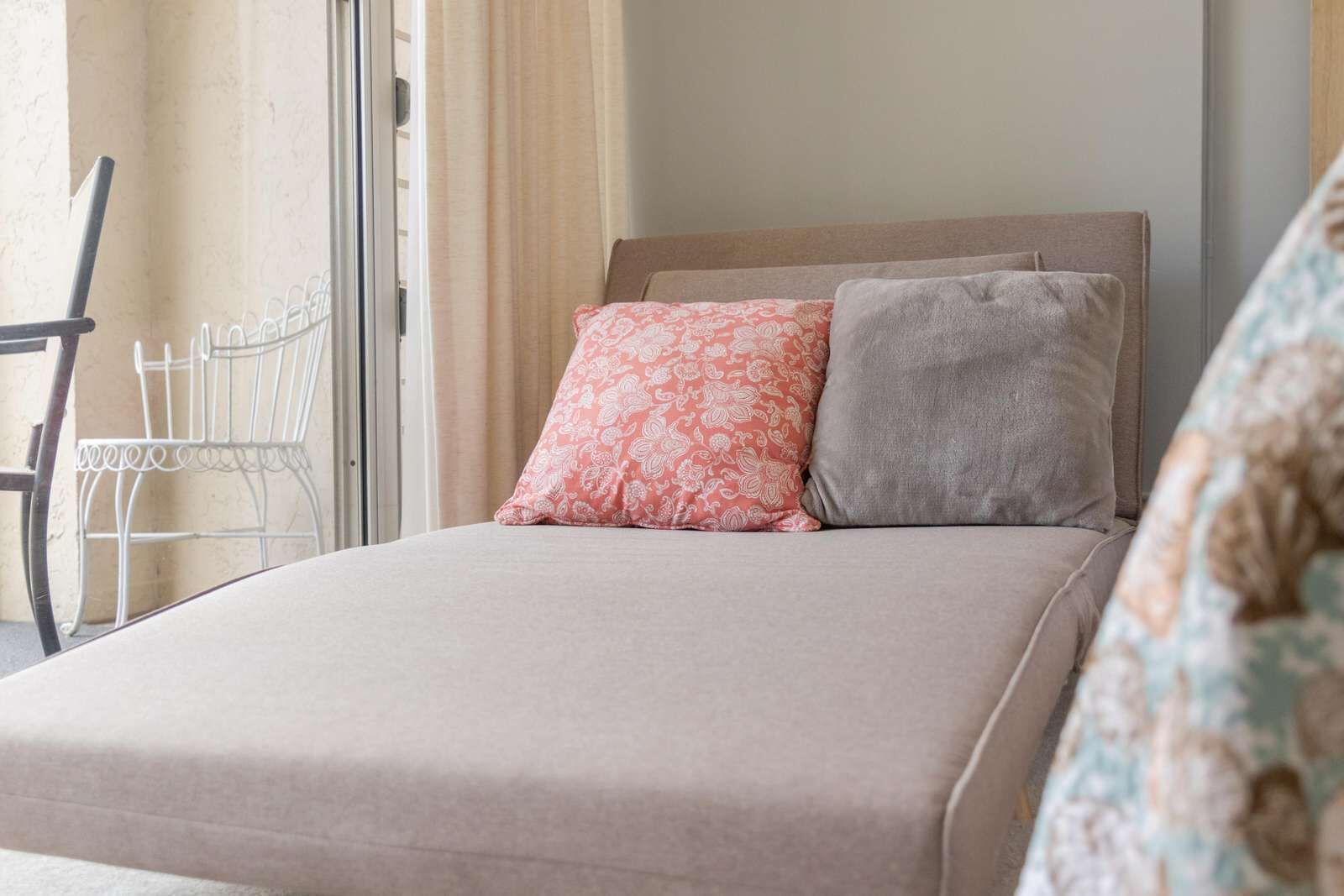 A bed with a headboard, two pillows, a chair, and a window with curtains.