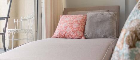 A bed with a headboard, two pillows, a chair, and a window with curtains.