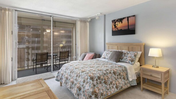 Une chambre à coucher comprenant un lit, une table de chevet, une chaise, une table et une vue sur l’extérieur grâce à une porte-fenêtre coulissante.