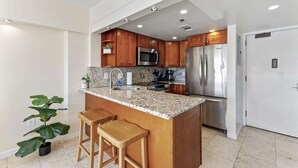 A modern kitchen with granite countertops, stainless steel appliances, wooden cabinets, and a central island with bar stools. - Ilikai 14th Fl Studio | City View | AC | Pool (Honolulu)