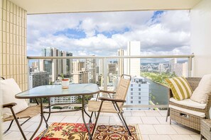 Un balcon avec une table en verre, des chaises en osier et une vue sur le paysage urbain.