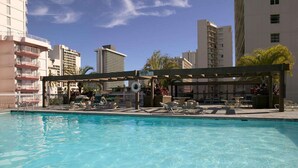 En swimmingpool med solstolar och ett avskärmat sittområde, omgiven av höga byggnader.