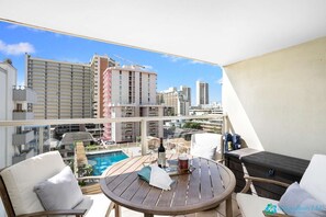 Een balkon met een houten tafel, twee witte stoelen, een klein zwembad en uitzicht over de stad.