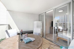 A balcony with a round wooden table, two white chairs, a wine bottle, and a glass. - Island Colony 9th Fl Studio - Pool View (Honolulu)