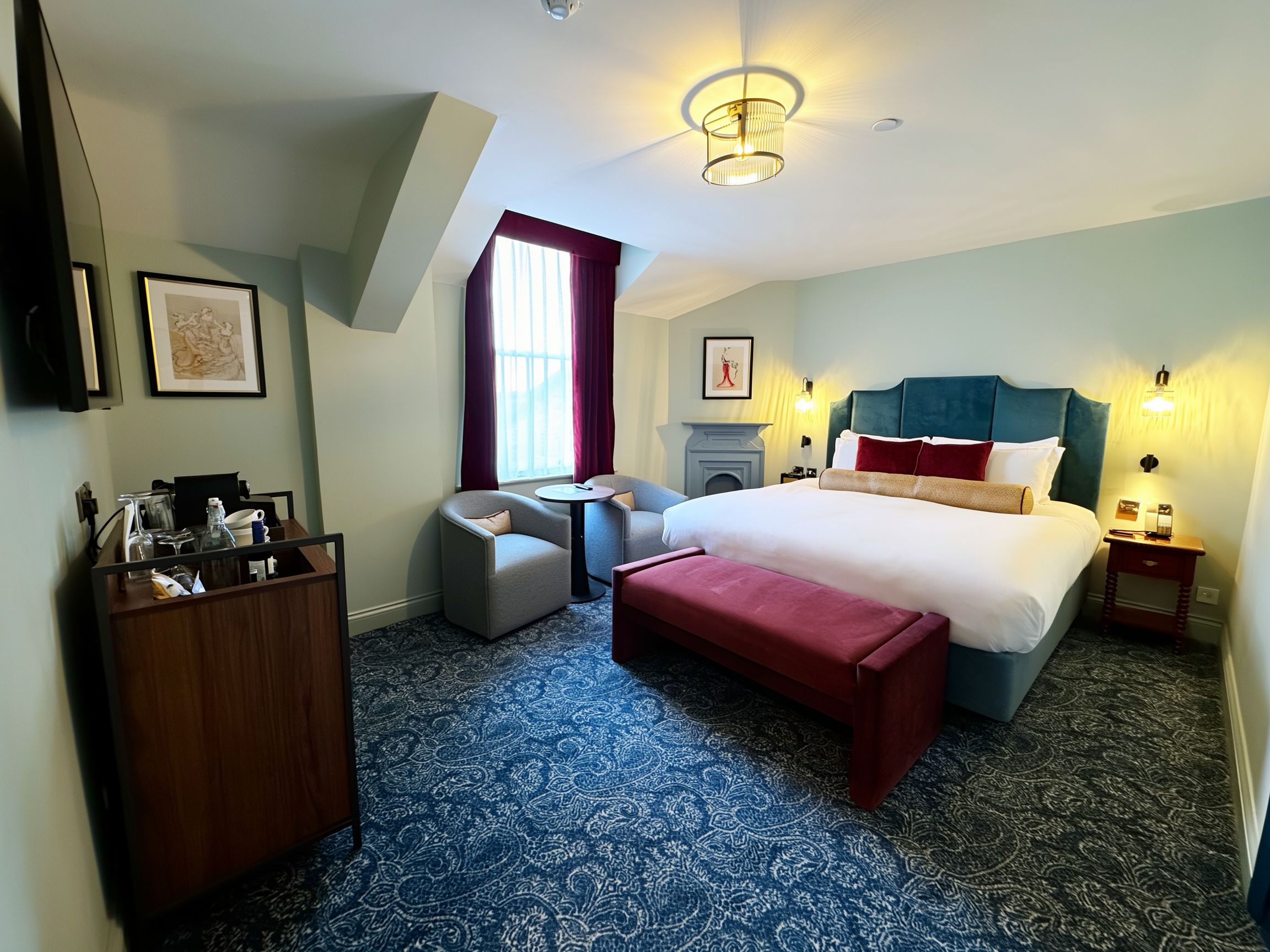 A hotel room with a bed, a desk, a chair, a fireplace, and a large window.