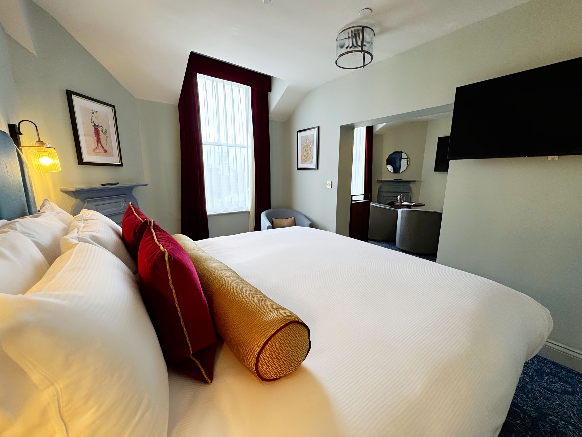 Habitación de hotel con una cama grande, un escritorio, una silla, un espejo y una ventana con cortinas.