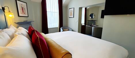 Habitación de hotel con una cama grande, un escritorio, una silla, un espejo y una ventana con cortinas.