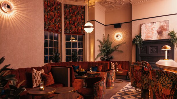 A cozy lounge area with a sofa, chairs, and a coffee table. There are potted plants and a fireplace. - The Royal Bell (Bromley)