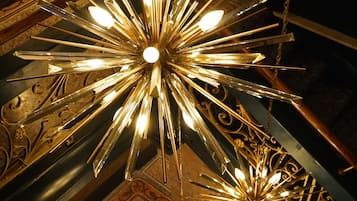 Un candelabro con múltiples fuentes de luz, suspendido del techo en una habitación con alfombra estampada y mobiliario.
