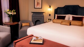 A hotel room with a large bed, a fireplace, a small table with a vase of flowers, and a chair. - The Royal Bell (Bromley)