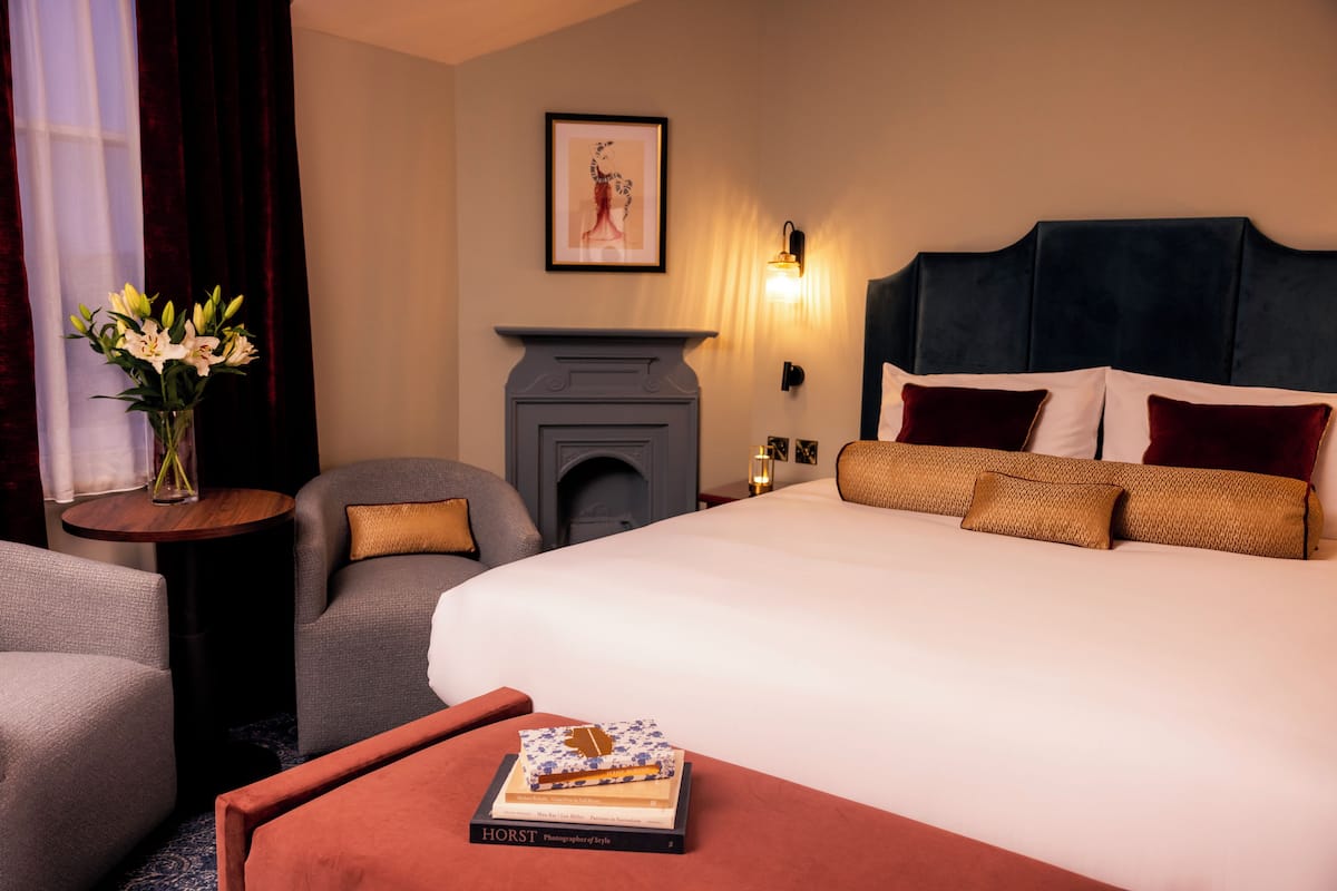 A hotel room with a large bed, a fireplace, a small table with a vase of flowers, and a chair.