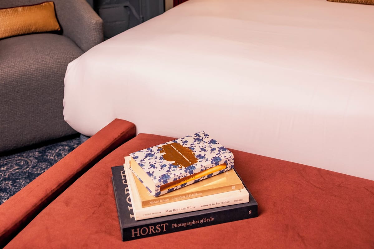 A hotel room with a large bed, a fireplace, a framed artwork on the wall, and a nightstand with a lamp.