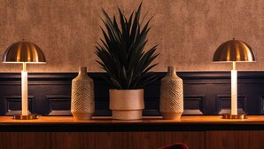 A room with a wooden counter, two lamps, a potted plant, and a red chair. - The Royal Bell (Bromley)