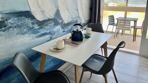 A room with a table set for tea, a painting of sailboats, and a view of a distant cityscape. - Sea view, calm and comfort in the village (Hyères)