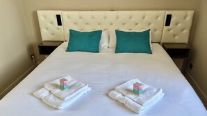 A hotel room with a large bed, two nightstands, and teal pillows. - Sea view, calm and comfort in the village (Hyères)