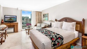 Habitación de hotel con cama, escritorio, televisor y vista a la ciudad.