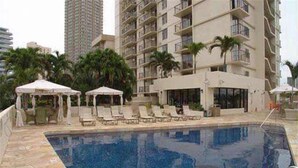 Una piscina con sillas de descanso y sombrillas, rodeada de edificios altos.
