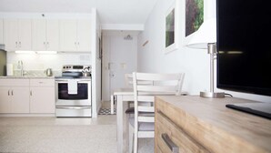 Cozinha moderna com armários brancos, fogão e área de refeições com mesa e cadeiras brancas.