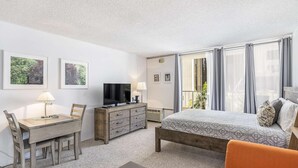 Quarto de hotel com cama, escrivaninha com cadeira, televisão e varanda com cortinas.