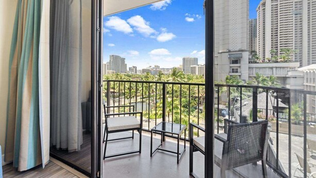 A balcony with a view of a cityscape, including high-rise buildings and palm trees. - 3rd Fl Palms Waikiki Studio Overlooking the Pool | Parking (Honolulu)