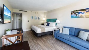 A hotel room with a bed, a blue sofa, a desk with a chair, and a TV on the wall. - 3rd Fl Palms Waikiki Studio Overlooking the Pool | Parking (Honolulu)