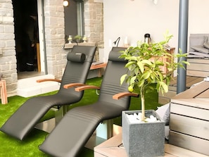 A spa area with two black lounge chairs, a small potted plant, and a stone wall. - 4 Apartments with Spa Area and Mountain Views (Oberibach)