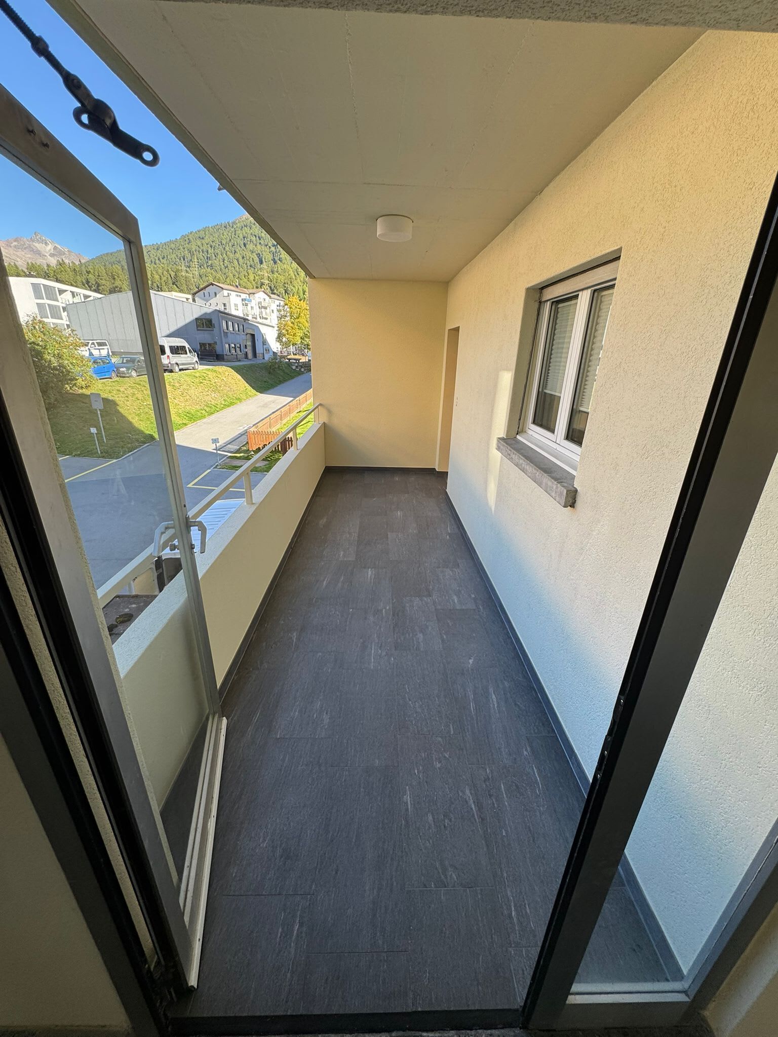 Un balcon étroit donnant sur un parking et des immeubles.