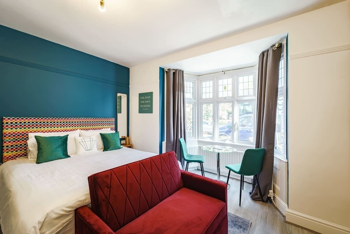 Een hotelkamer met een bed, een rode bank, een klein tafeltje en een raam met gordijnen.
