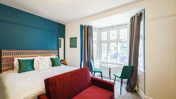Een hotelkamer met een bed, een rode bank, een klein tafeltje en een raam met gordijnen.
