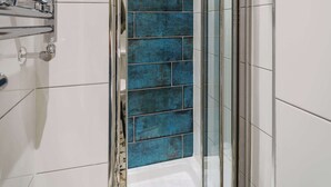 Una ducha con puerta de vidrio, paredes cubiertas de azulejos blancos y una pared decorativa con azulejos azules.