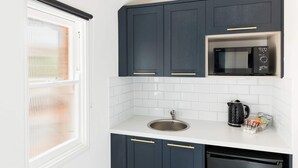 Una cocina con armarios oscuros, una encimera blanca, un lavamanos de acero inoxidable, un hervidor negro y un microondas.