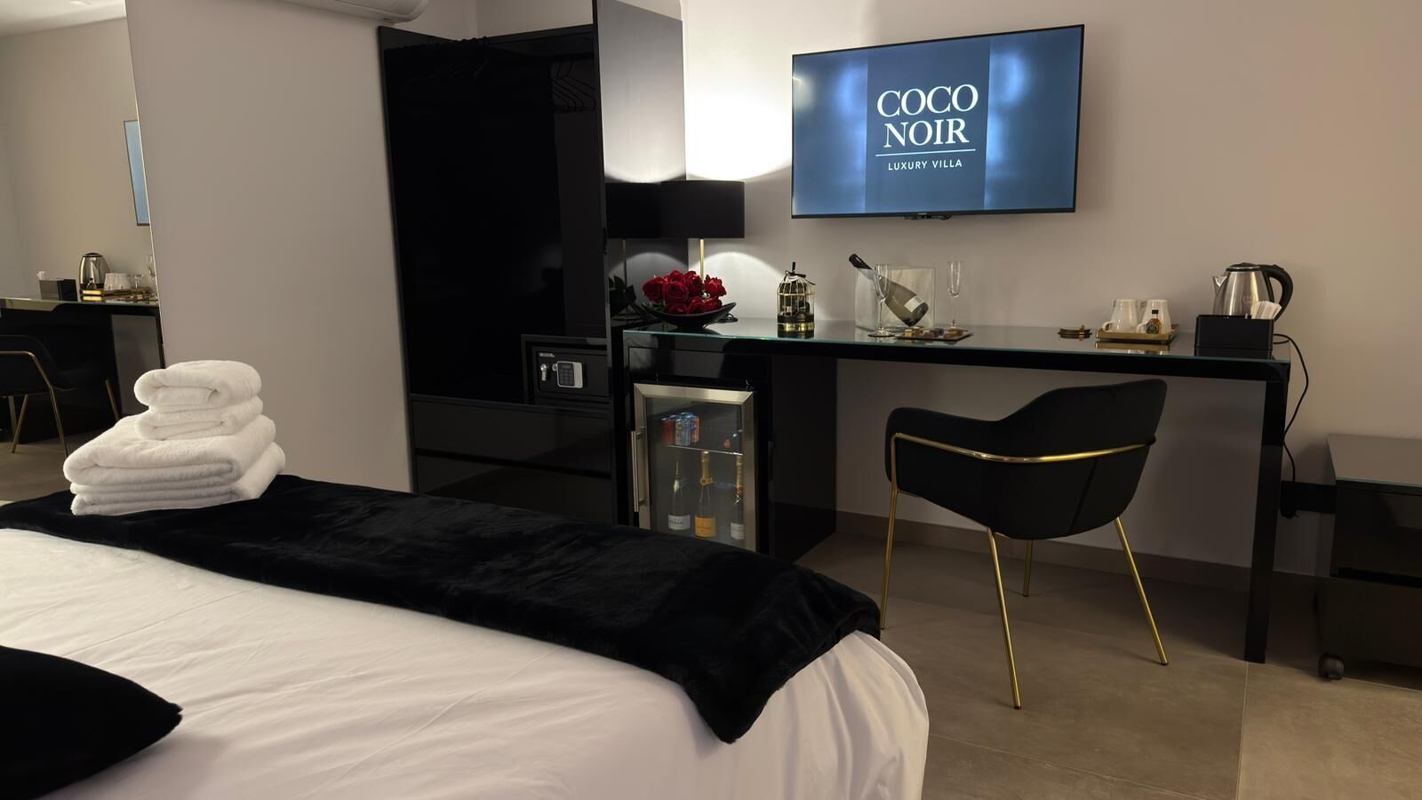 Habitació d'hotel amb un llit, una taula de treball, una cadira, un televisor i un minibar.