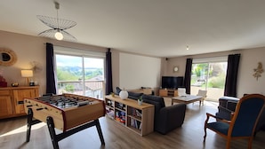Een ruime woonkamer met een tafelvoetbalspel, een bank, een televisie en een balkon met uitzicht.