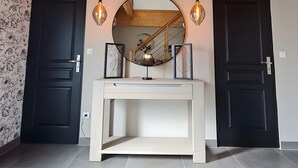 Een modern interieur met een houten plafond, een ronde spiegel, twee zwarte deuren, een witte console tafel en twee hangende pendellampen.