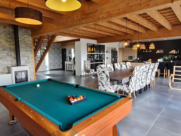 Une table de billard avec des billes, un coin repas avec des chaises à motifs et une cuisine équipée d’appareils électroménagers modernes.